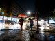 Pessoas com guarda-chuva caminham sob chuva em rua de cidade brasileira